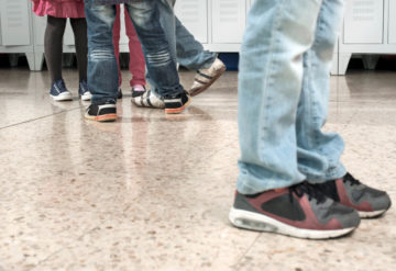Kids shoes in hallway showing one boy standing alone by a group.