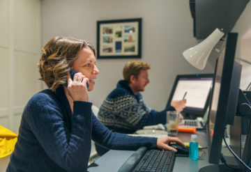 Researcher talking on phone and working on computer at home.